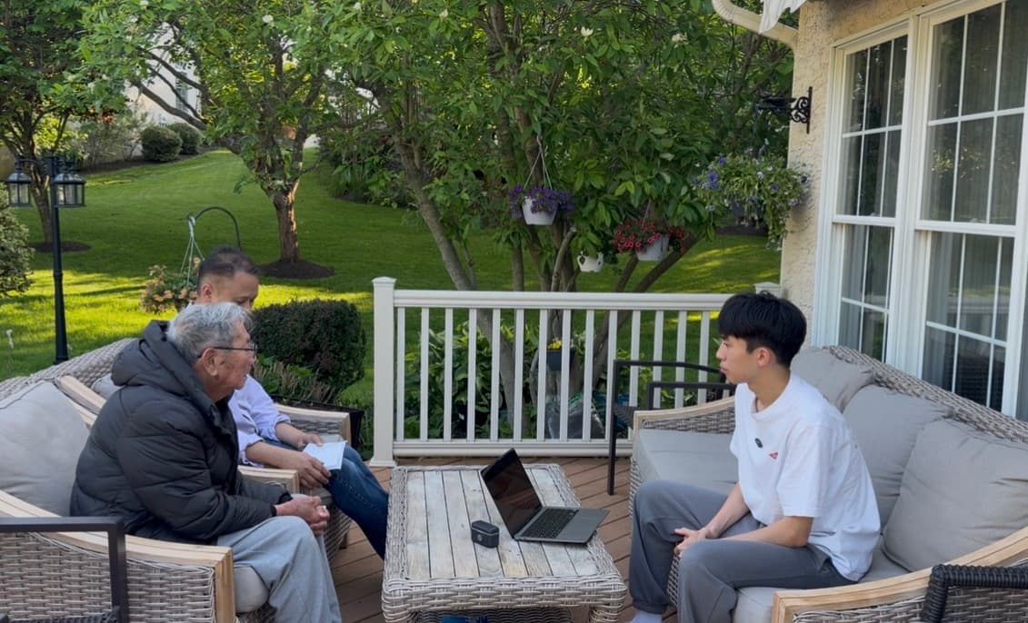 A volunteer helping a senior with a laptop on an outdoor patio